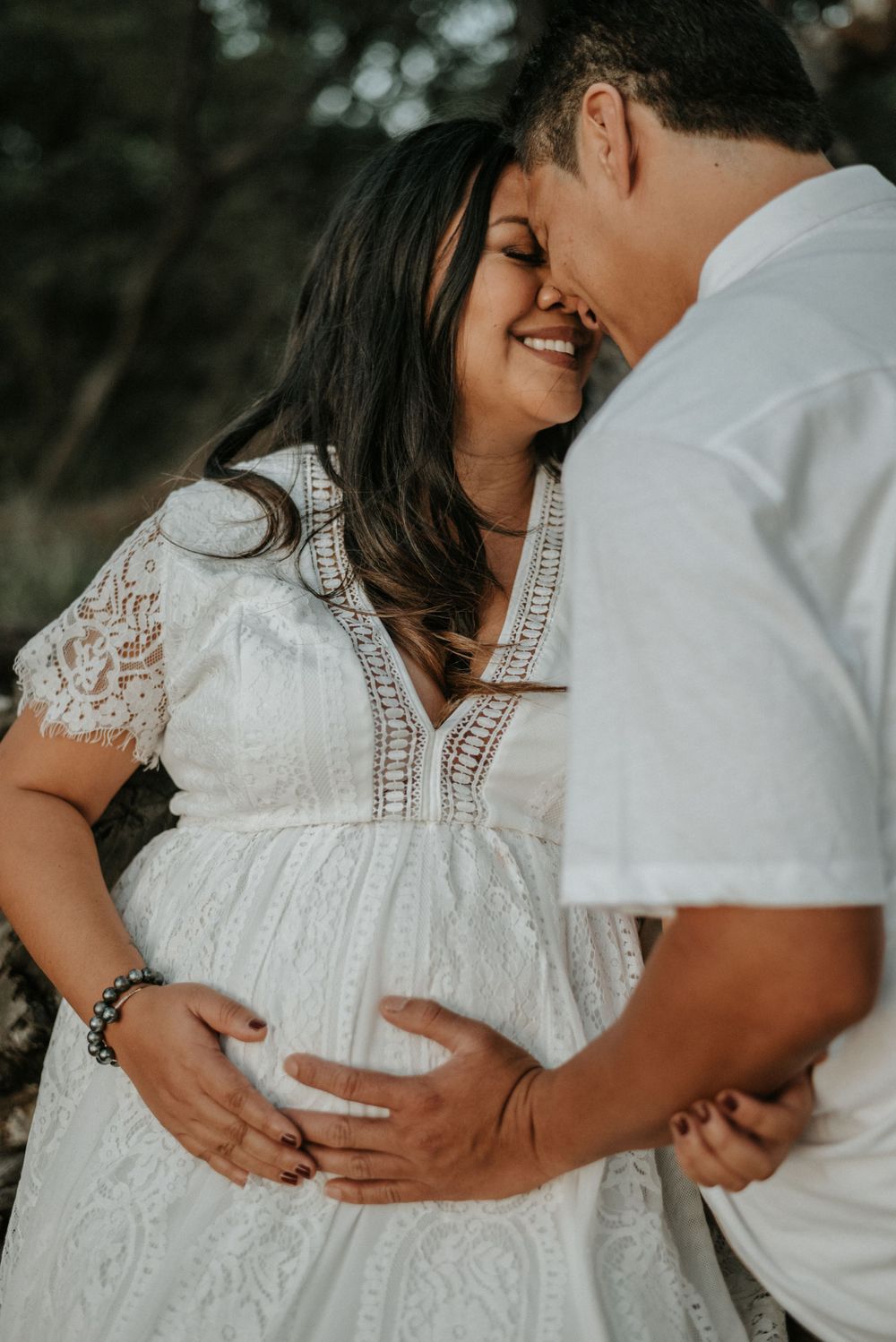 Intimate beach maternity photos showing couple embracing in white attire against natural backdrop.