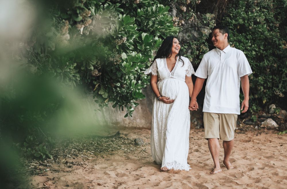 Couple walking hand in hand on beach with tropical foliage in background.