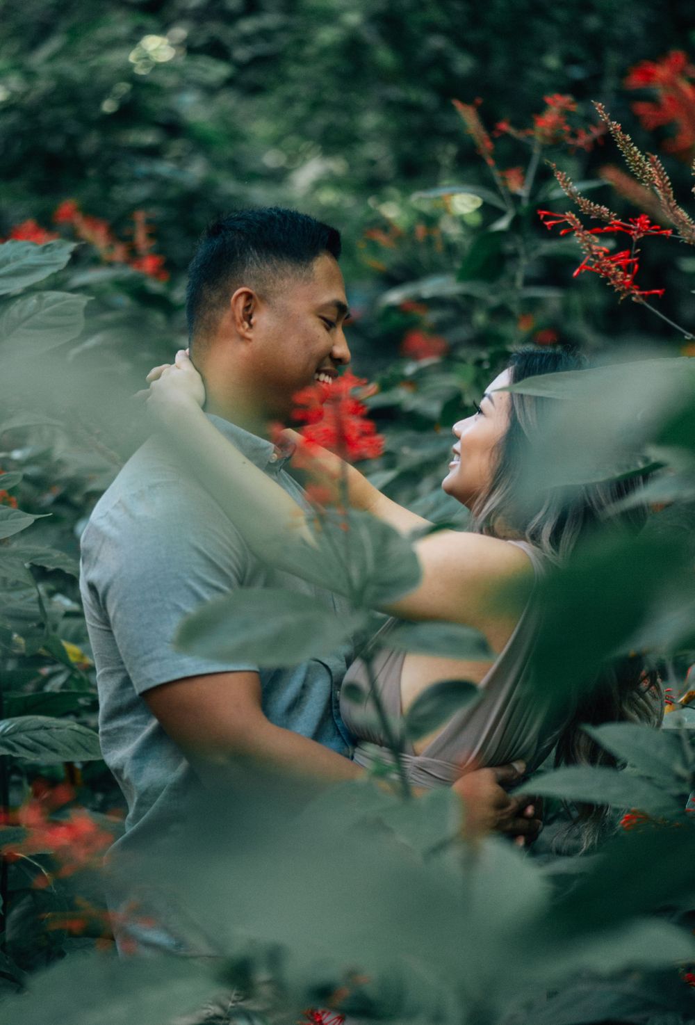 Red flowers frame an intimate scene between two people in a garden setting.
