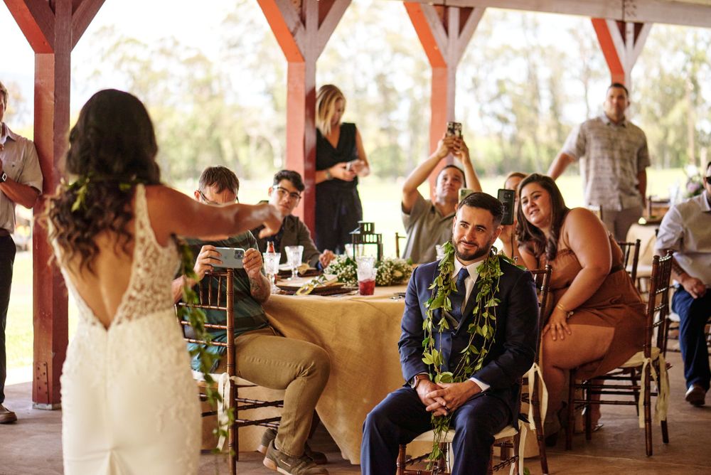 Wedding reception celebration in a covered outdoor venue with rustic wooden beams and elegant table settings.