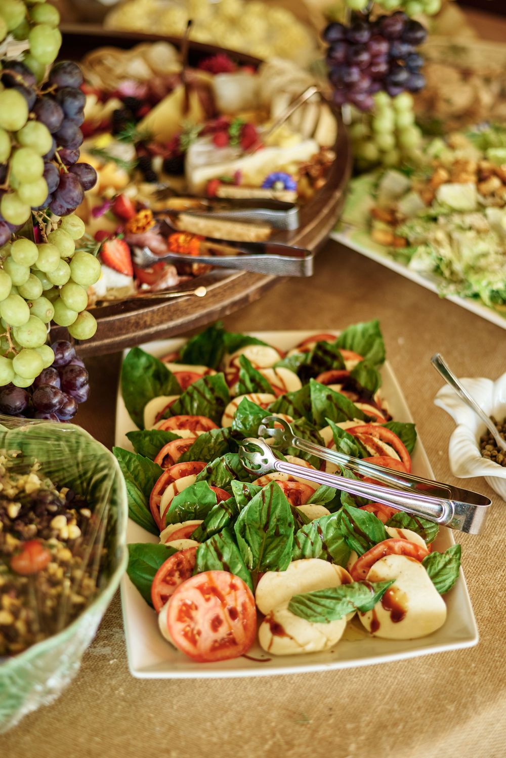 Fresh appetizer platter with grapes, tomatoes, salad greens and garnishes arranged on white plates.