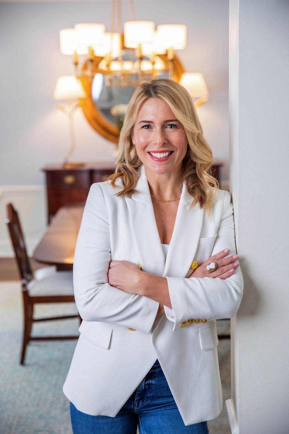 Professional woman in white blazer standing confidently in elegant dining room.