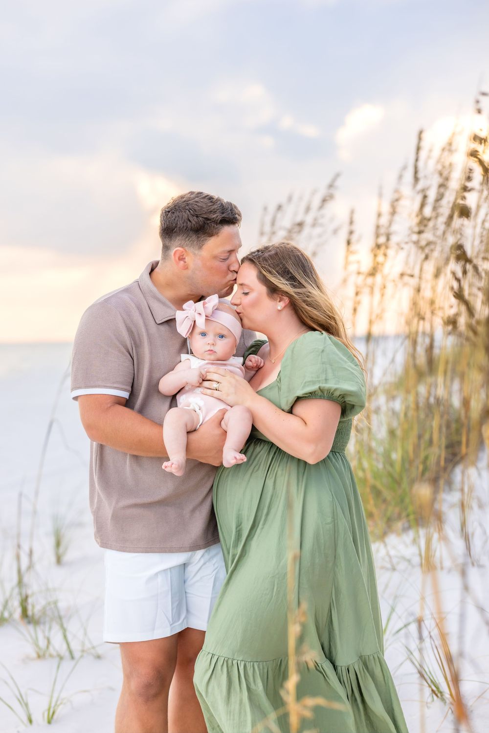 Family shares tender moments together on a sandy beach with sea oats during golden hour sunset.