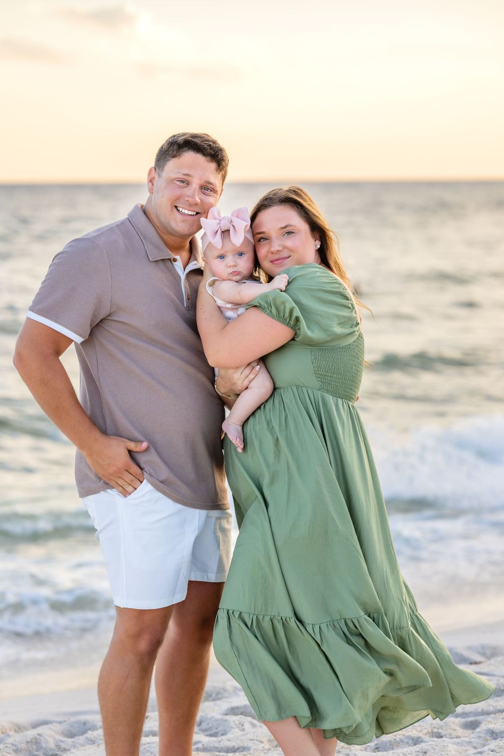 A couple shares joyful moments on a sandy beach at sunset wearing grey and green outfits.
