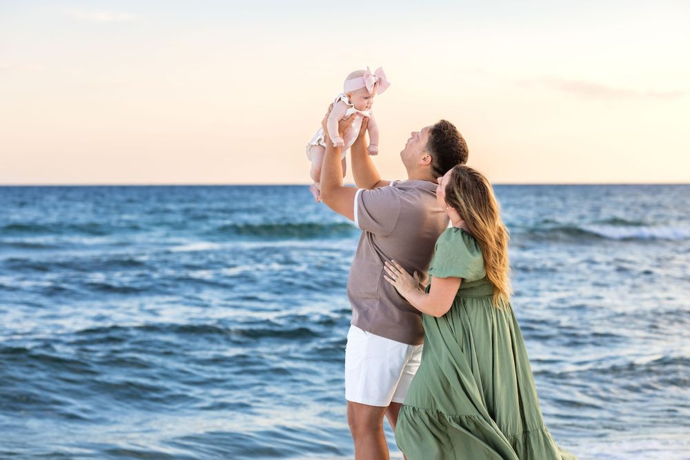 Couple embraces on a sandy beach at sunset with ocean waves in the background.