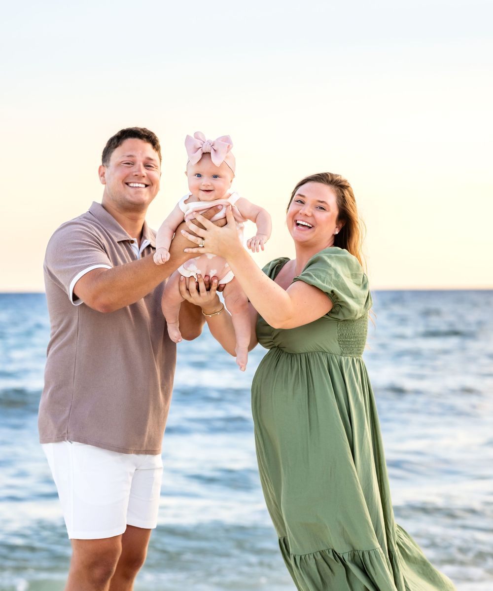 Couple in casual attire sharing playful moments together at sunset on a beach with ocean waves in background.