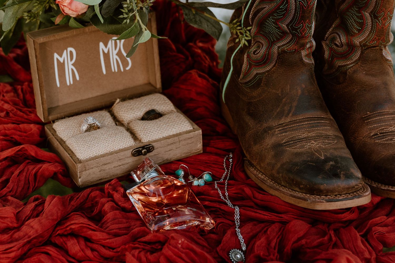 Wedding detail photo of rustic brown boots and Mr & Mrs sign with red floral accents.