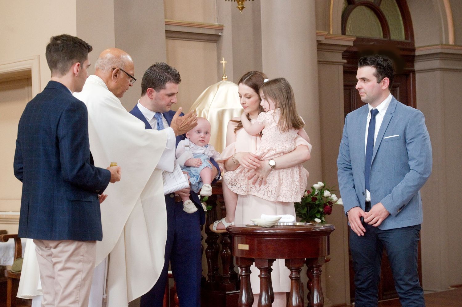 Church baptism ceremony with family and clergy gathered at the altar.