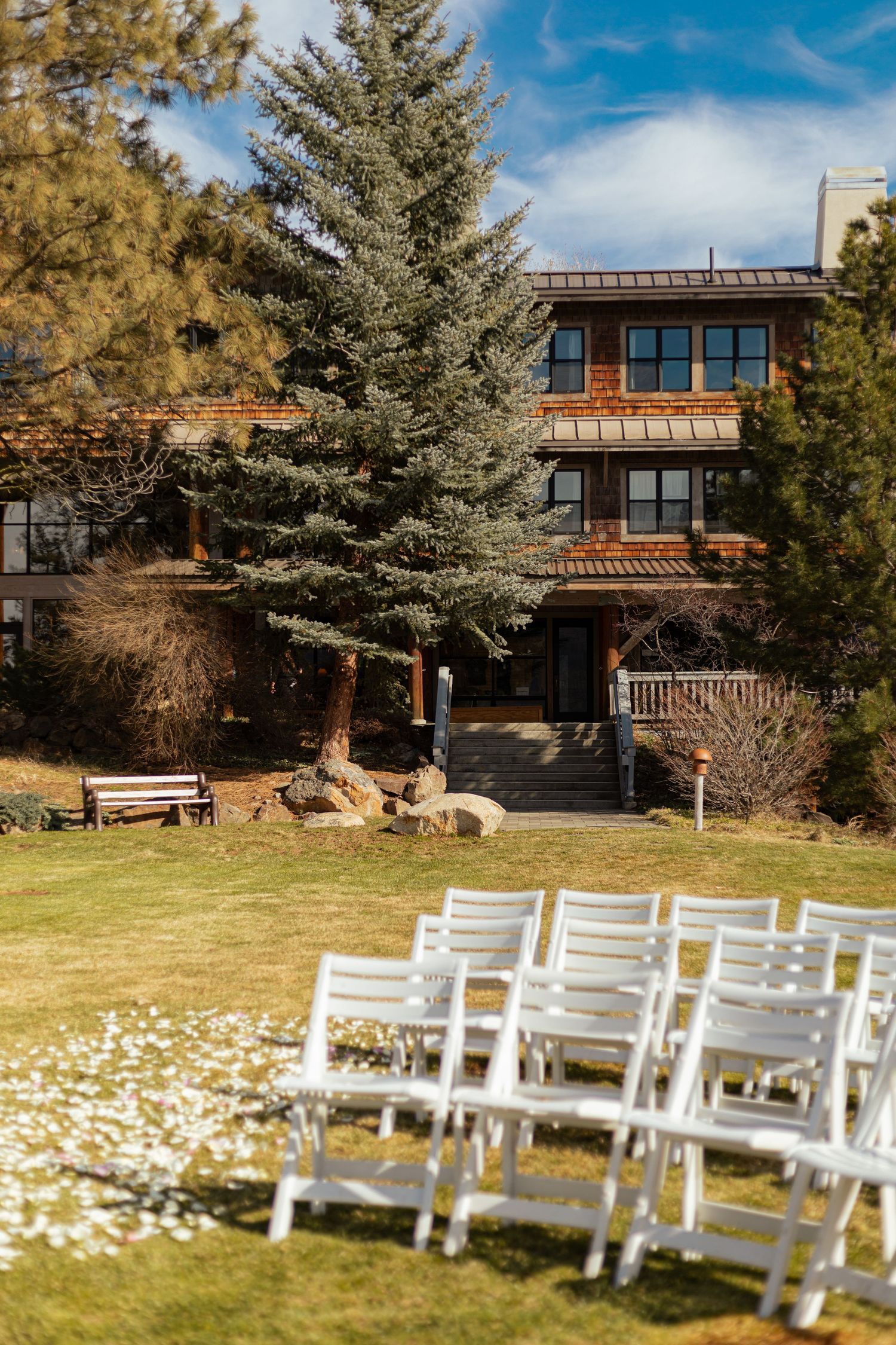 White wooden chairs arranged for an outdoor wedding ceremony with evergreen trees and a rustic lodge in the background.
