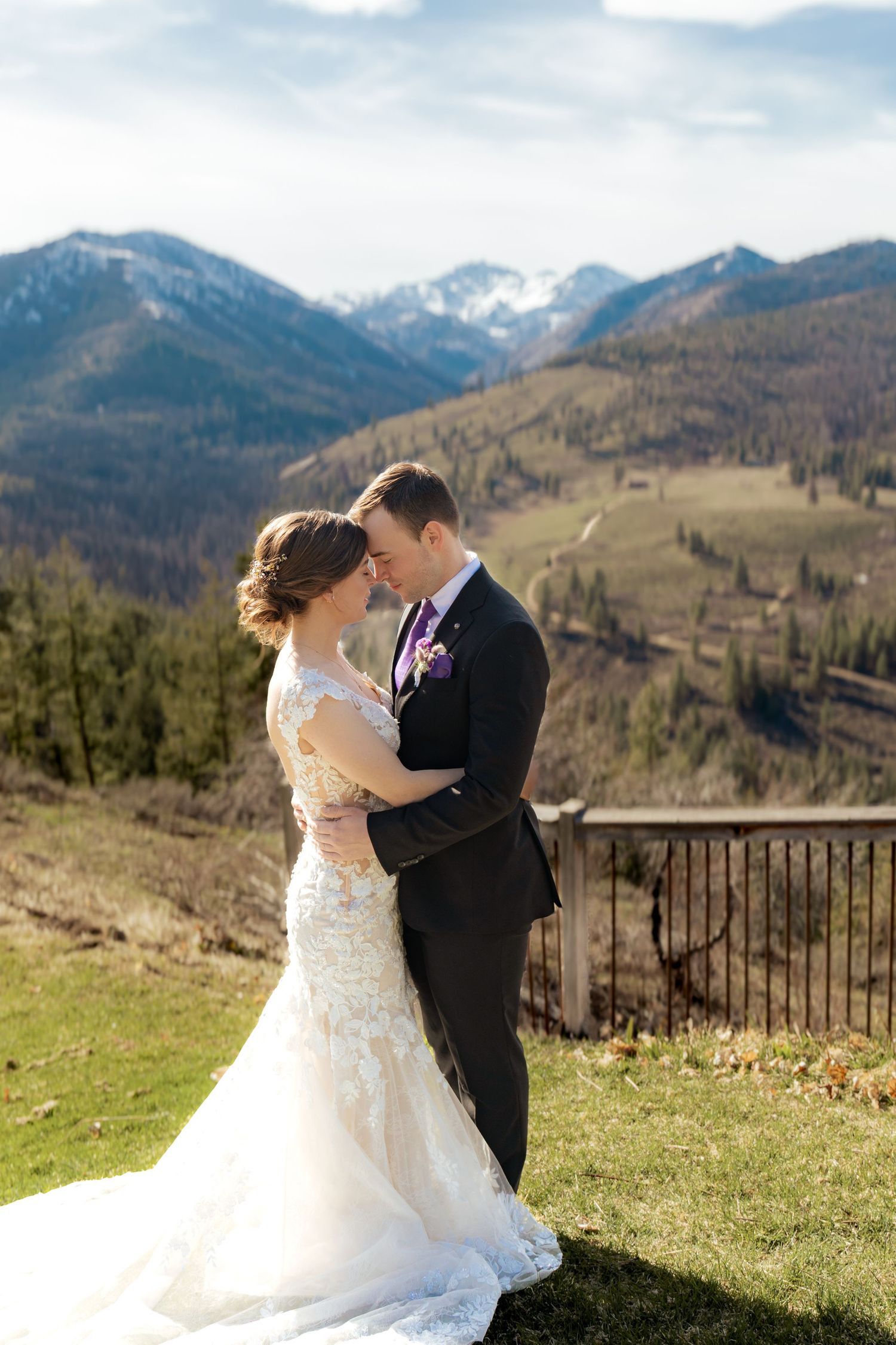 Newlyweds share tender moments on a mountain viewpoint surrounded by majestic peaks and spring grass.