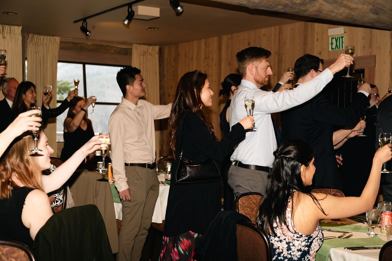 Party guests raise their glasses in a celebratory toast at an indoor event.