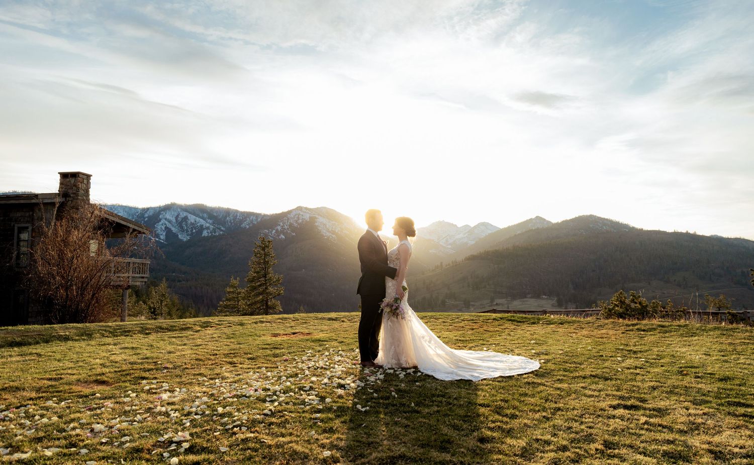 Panoramic mountain landscape with dramatic sunset skies over snow-capped peaks and rolling meadows.