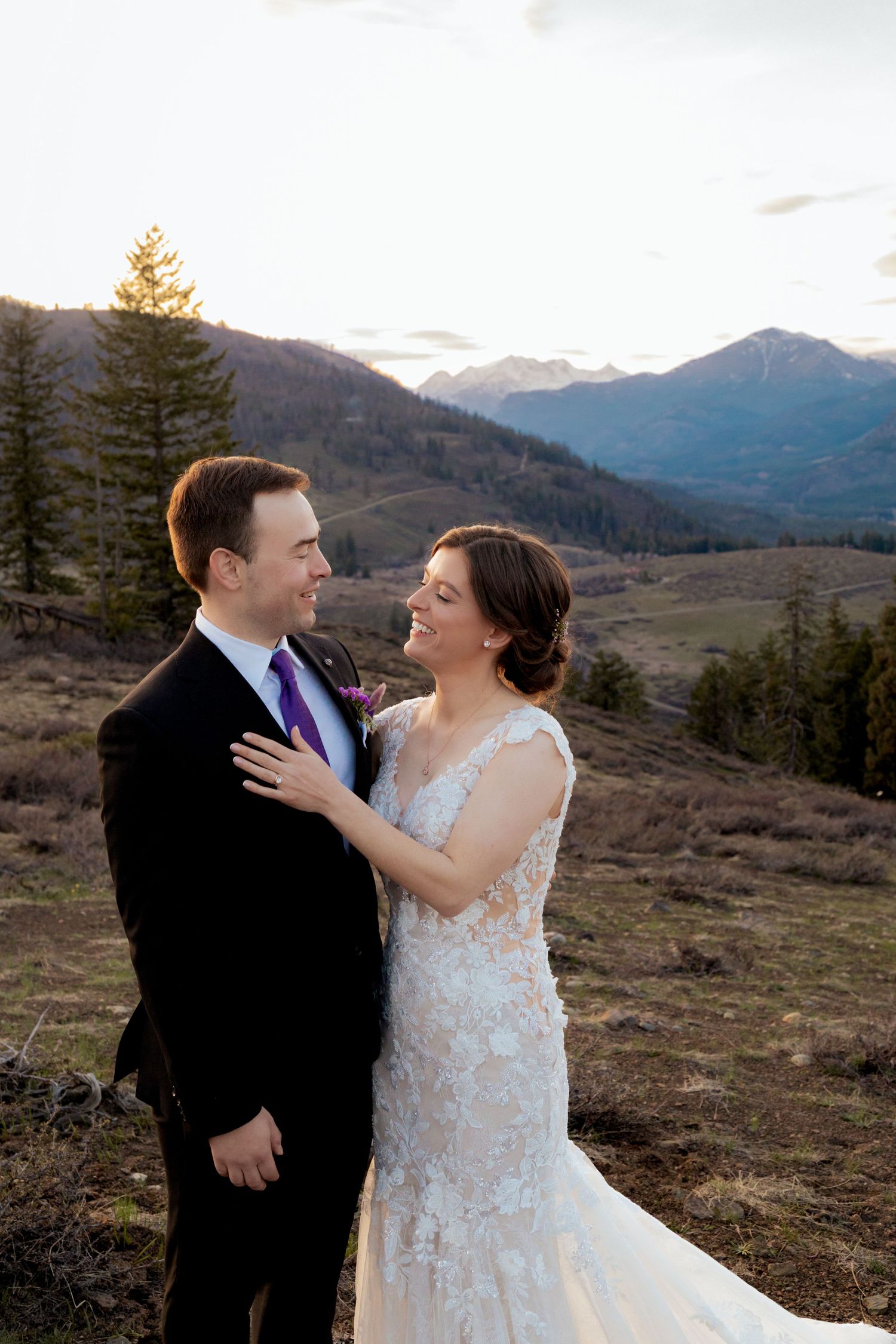 A couple in wedding attire shares an intimate moment against a backdrop of snow-capped mountains at sunset.