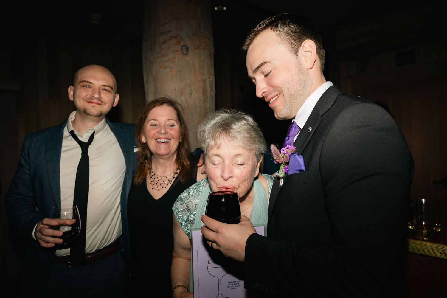 A group of formally dressed people interact and mingle at a dimly lit indoor gathering.