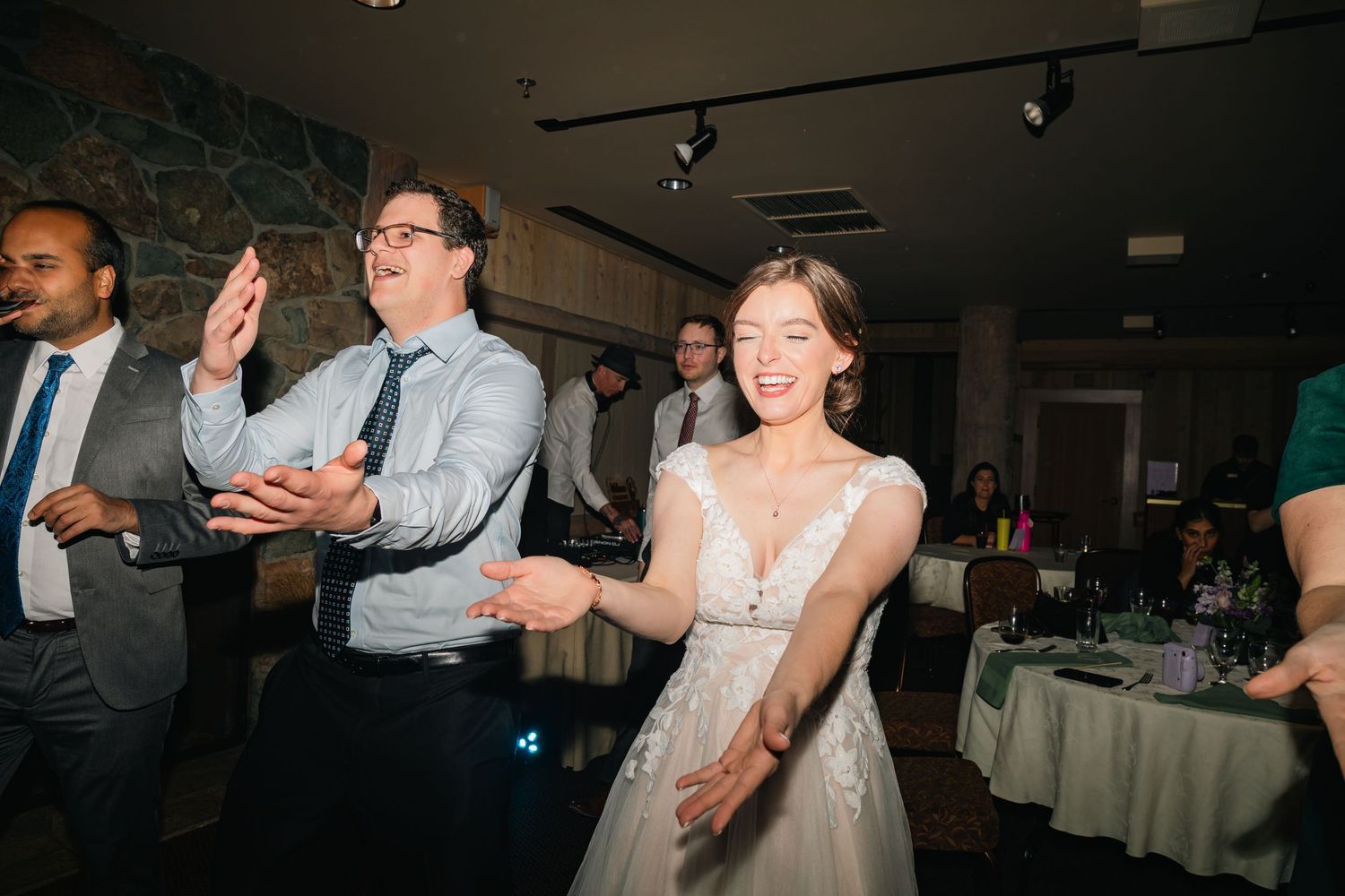 Wedding guests dance and celebrate together on a dimly lit dance floor at a reception party.