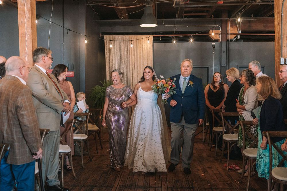 Wedding guests dance and celebrate together on a rustic wooden dance floor at an indoor reception venue.