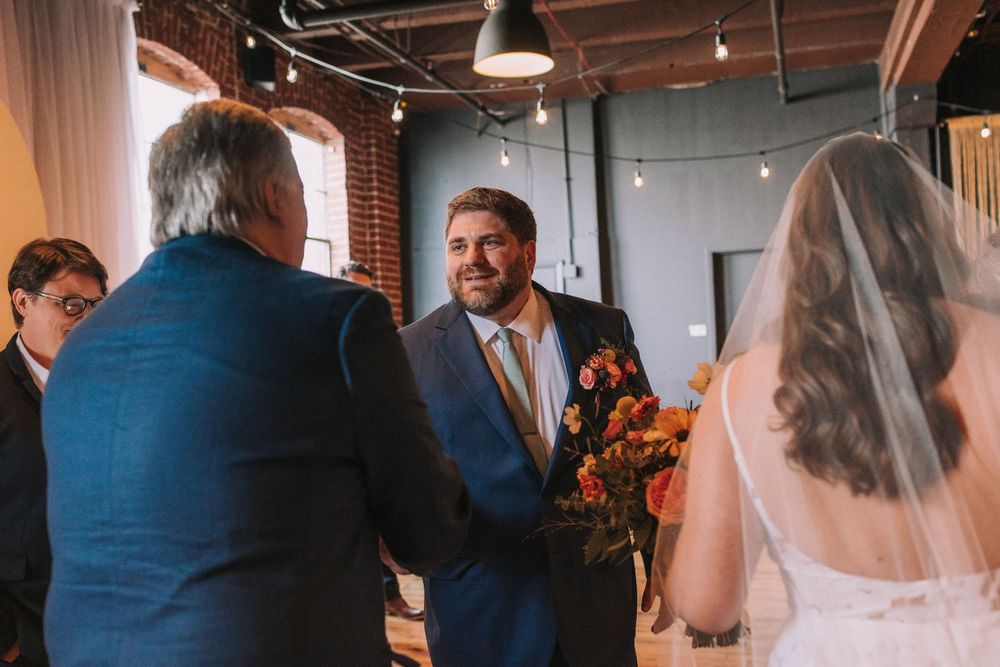 Wedding ceremony processional with bridesmaids and groomsmen walking down the aisle in an industrial venue.