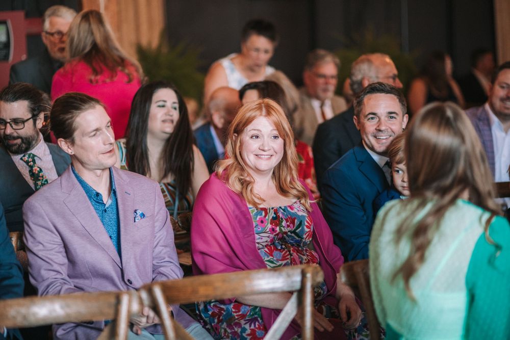 Wedding guests smile and laugh during a joyful moment at an indoor celebration event.