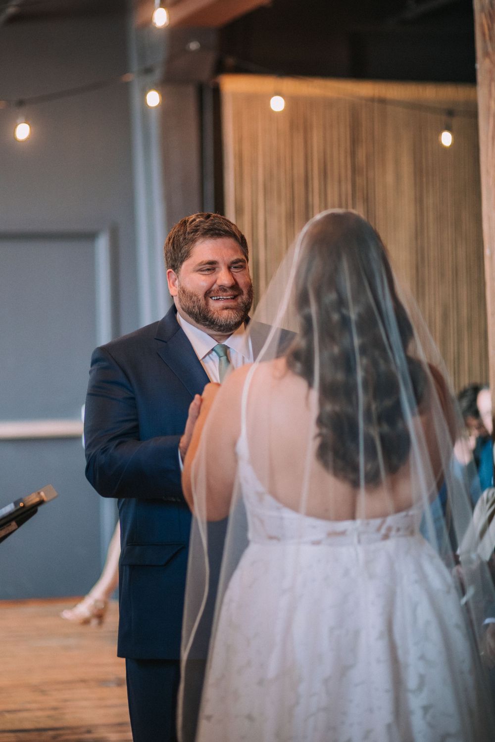A sequence of intimate first look moments between a bride and groom in an indoor venue with hanging lights.