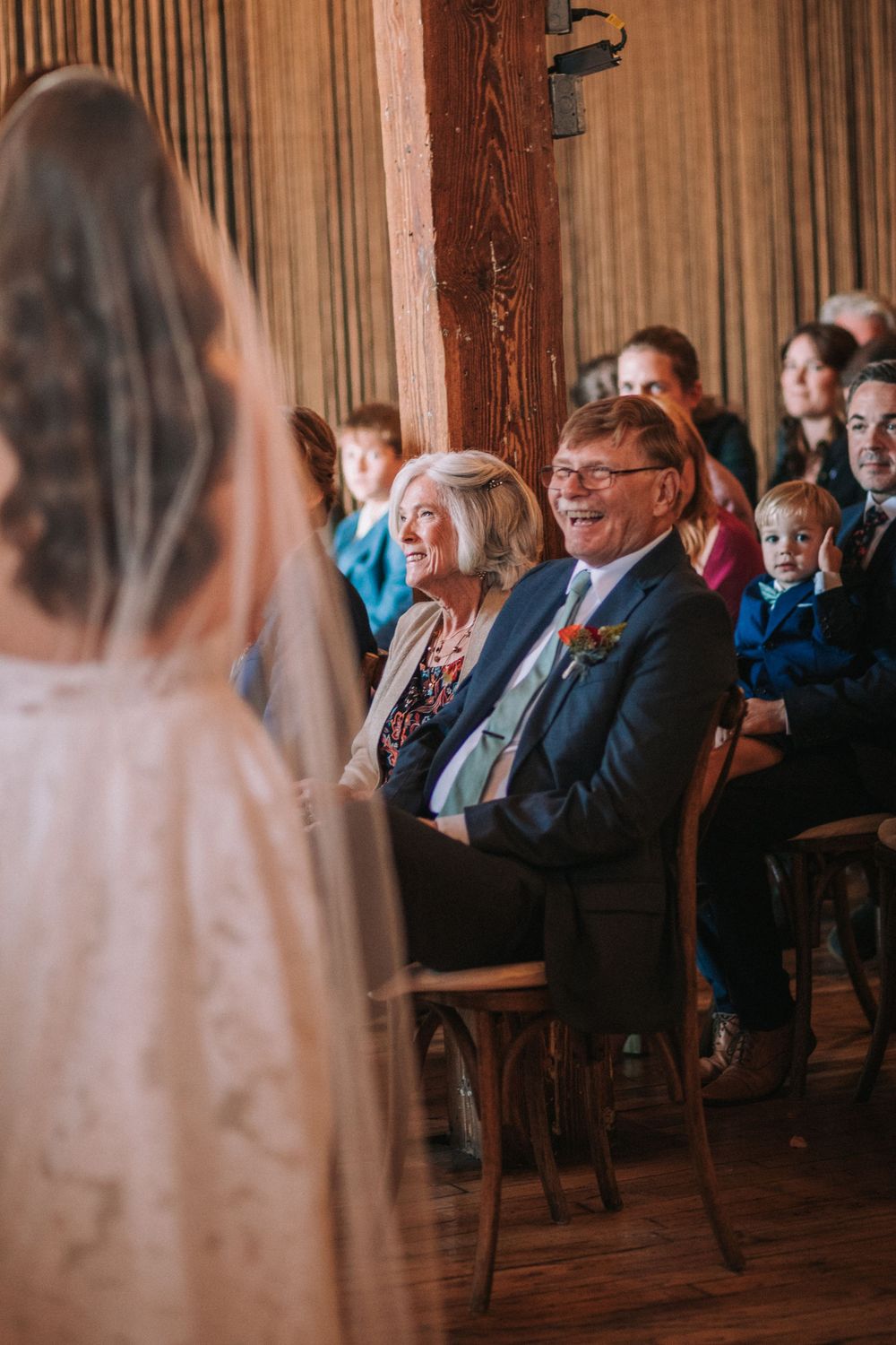 Wedding guests smile and laugh during an emotional moment in a rustic wooden venue.
