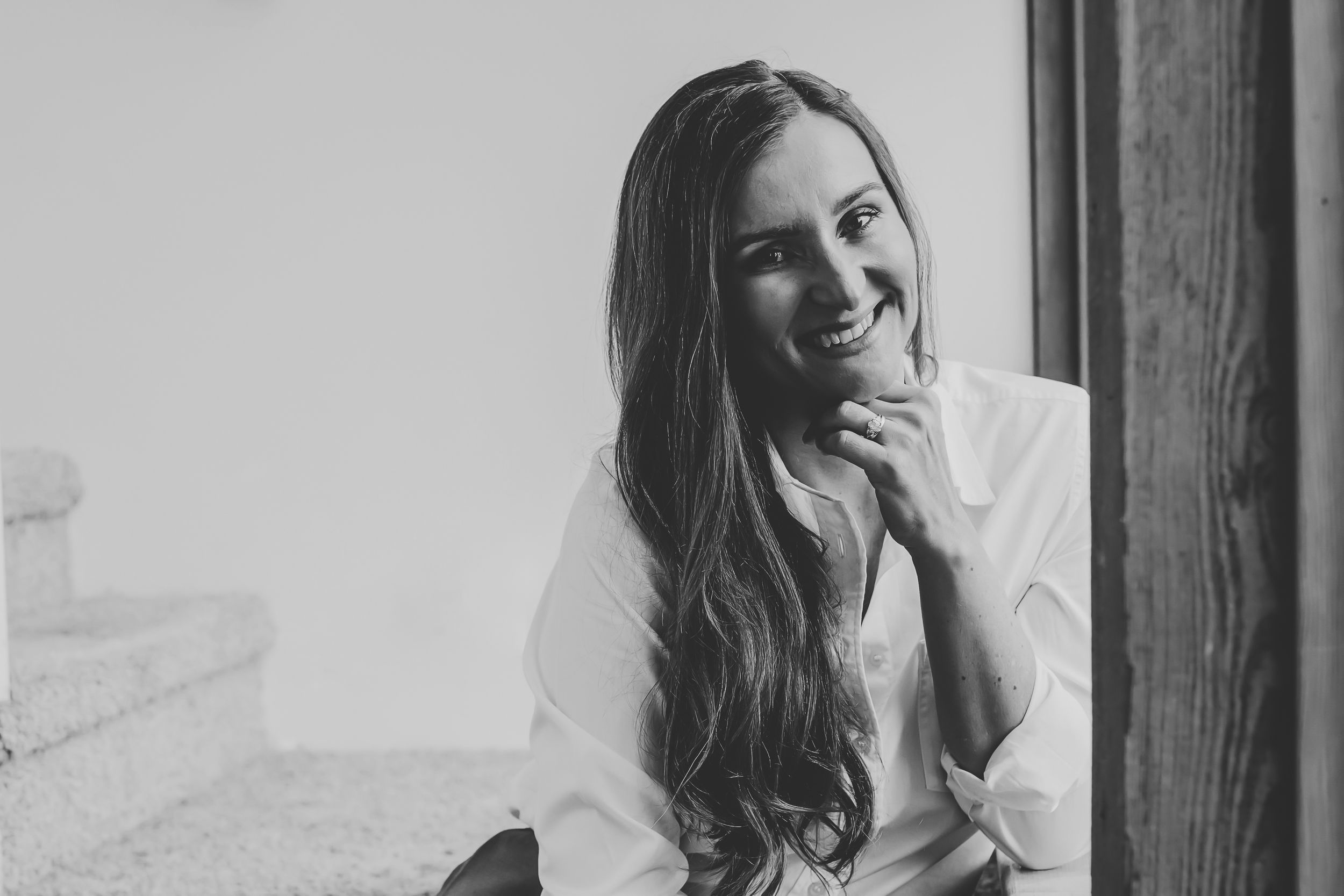 A series of black and white portraits showing a person with long dark hair laughing and smiling against a wall.