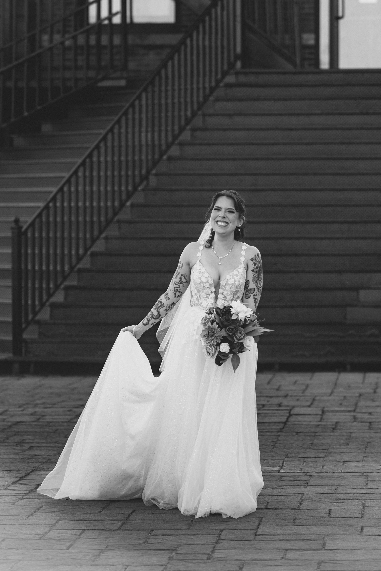 A bride in a flowing white wedding dress twirls and spins joyfully on a cobblestone street.
