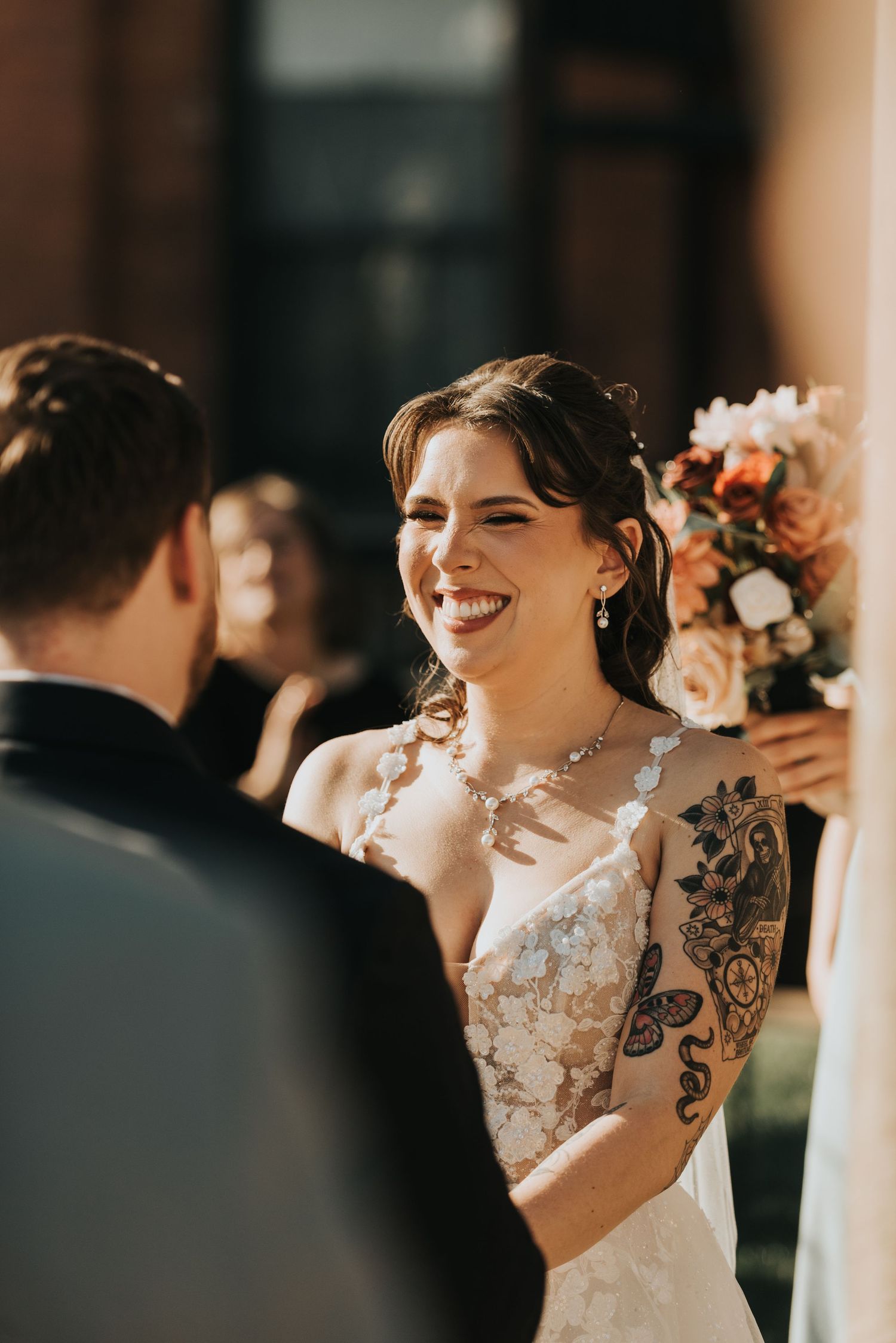 A bride in a white lace dress smiles joyfully during an intimate wedding ceremony moment.