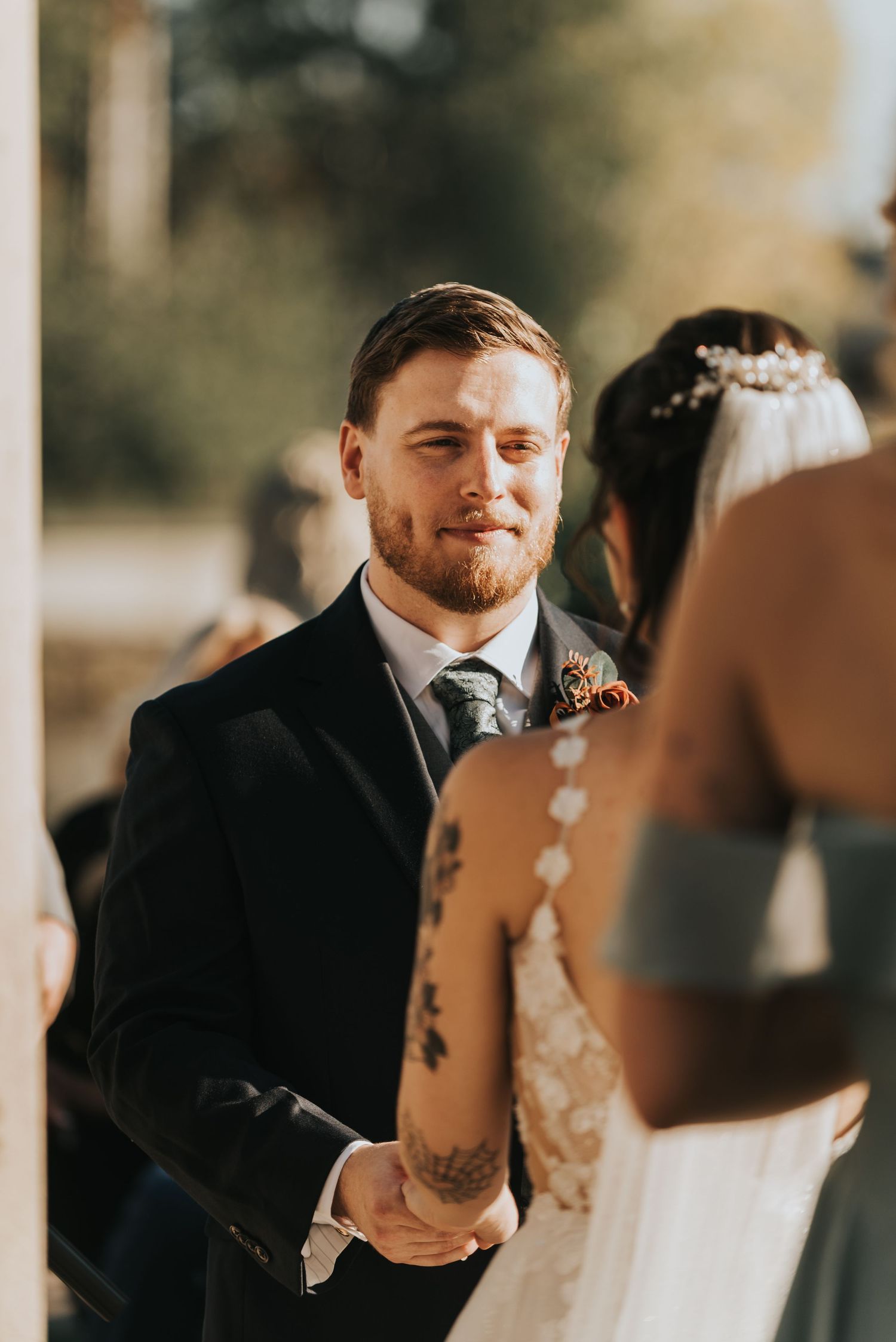 A groom in a black suit shares an emotional reaction during a wedding ceremony.