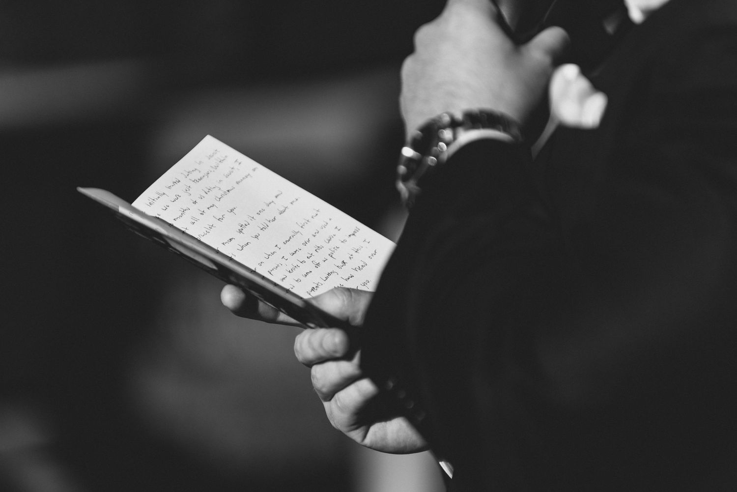 A person holds a small book or paper with handwritten text in black and white.