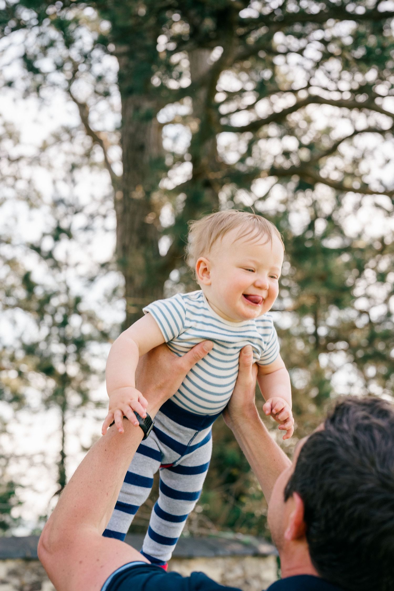 Lifestyle family photography of a parent lifting their baby outdoors, photographed naturally during an unposed family session