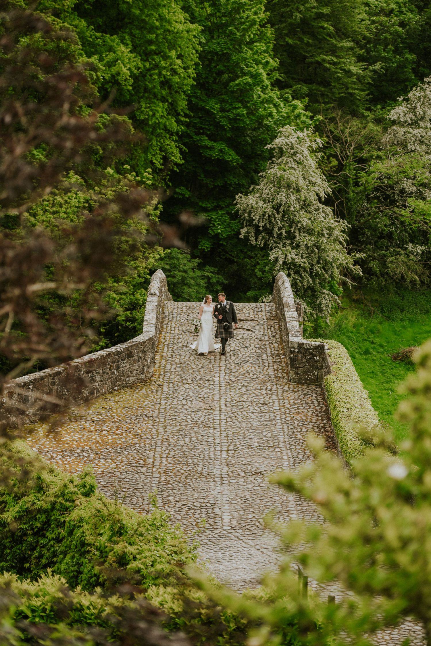 A couple embraces in a garden setting with a flowing white veil and Burns Monument visible from Brig o' Doon Ayrshire wedding photography