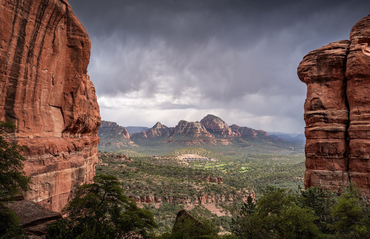 Dramatic panoramic view of red rock formations in Sedona Arizona under stormy clouds with distant mountain peaks.