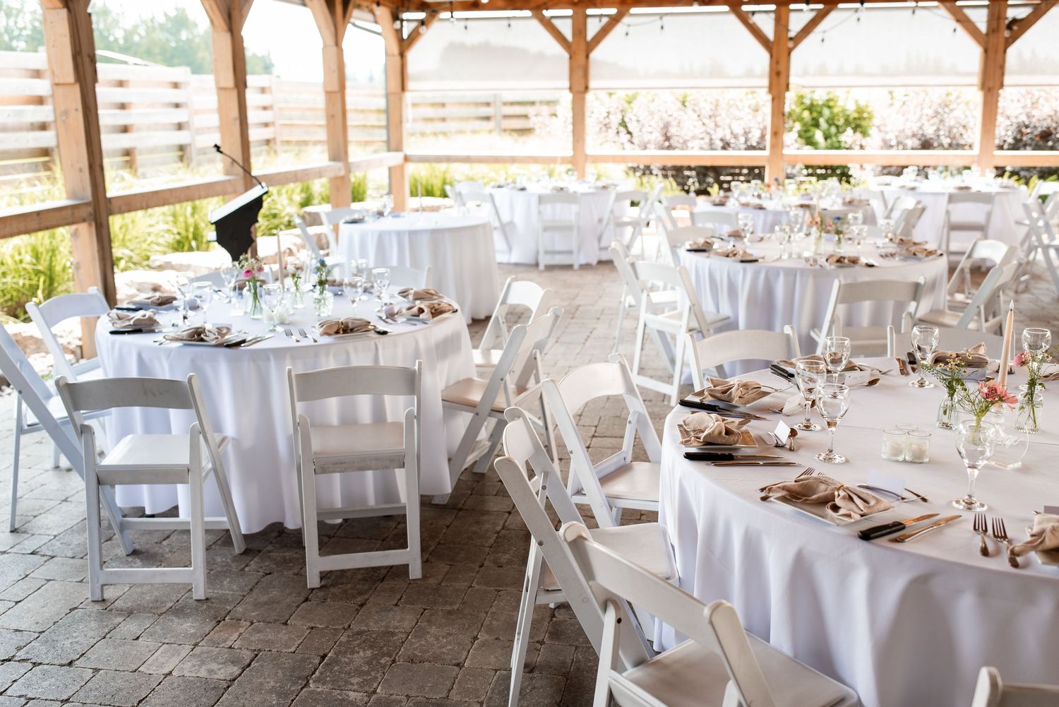 Elegant outdoor wedding reception at Strathroy Caradoc Sands Golf Club with white tables and chairs under wooden beams and string lights.