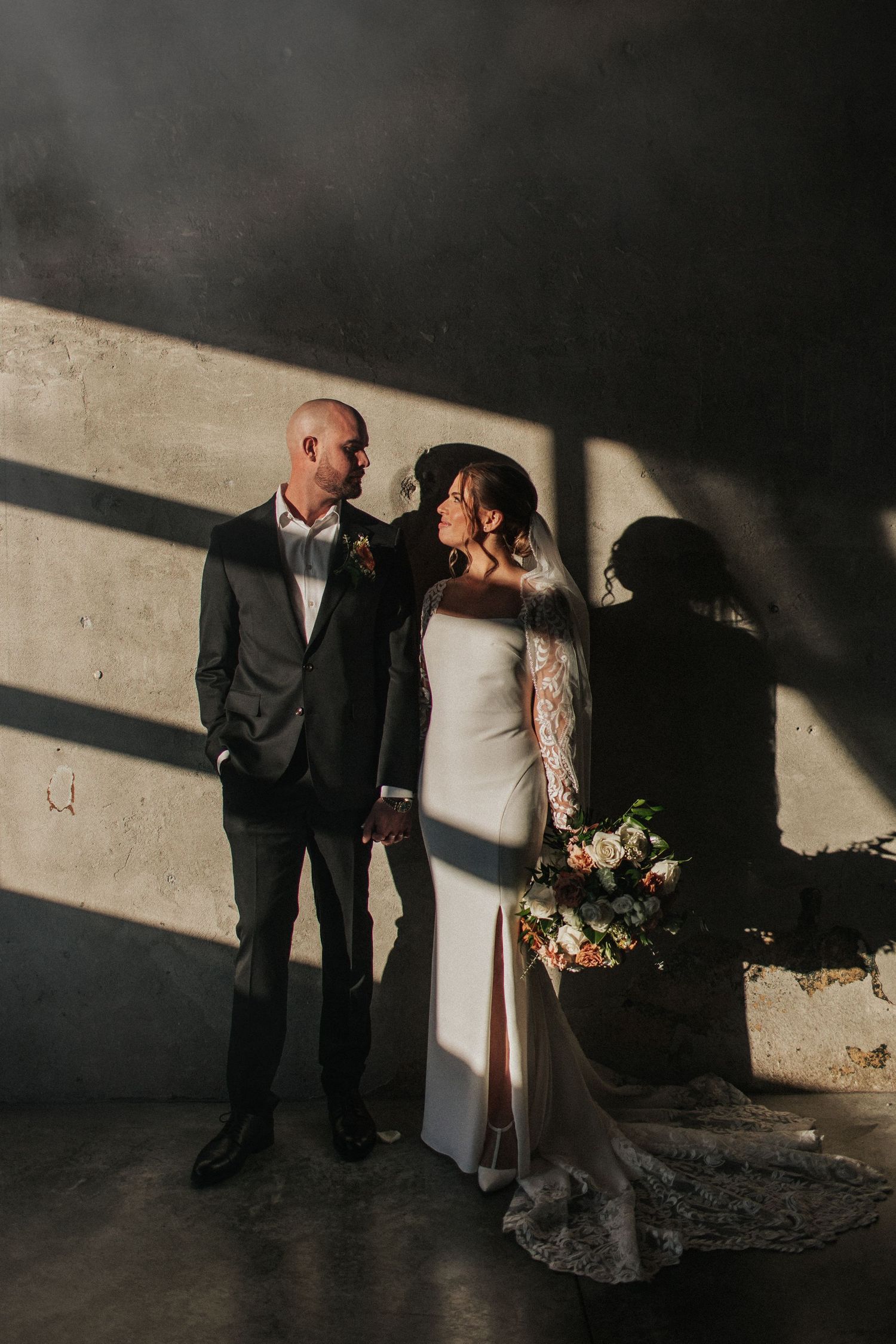 Artistic wedding photography utilizing dramatic lighting and shadows against an industrial wall.