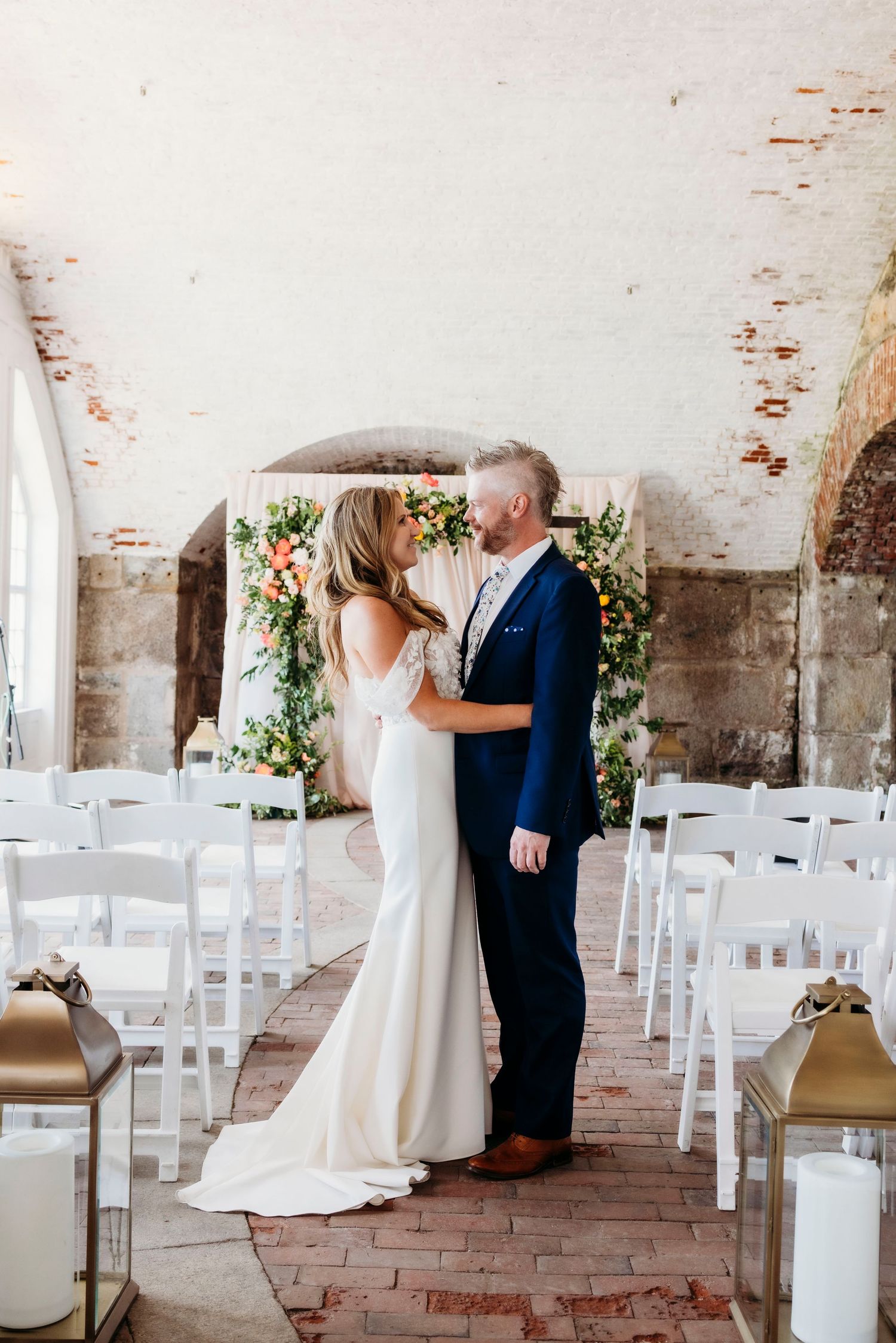 Elegant indoor wedding ceremony setup with white chairs and exposed brick walls in rustic venue.