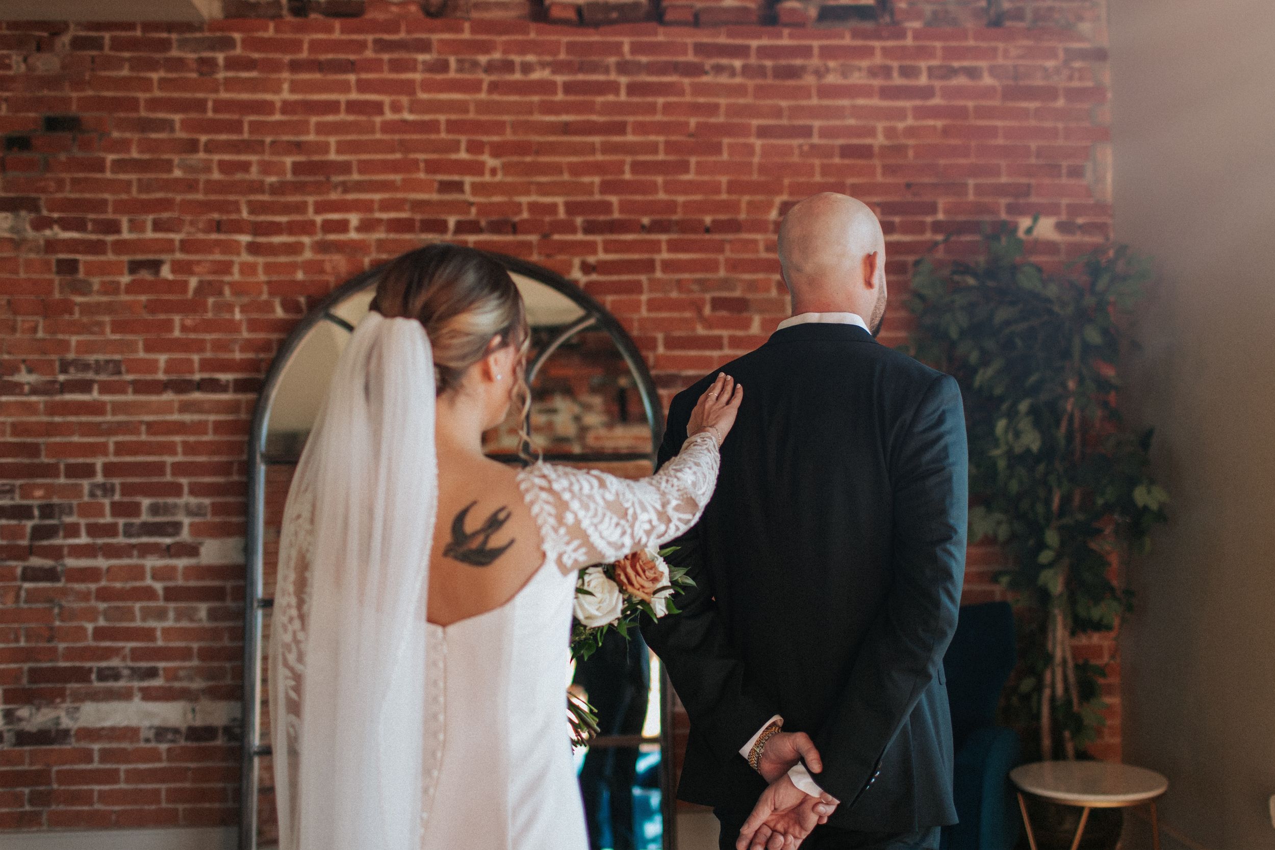 Emotional first look between couple in front of rustic brick wall with natural lighting.