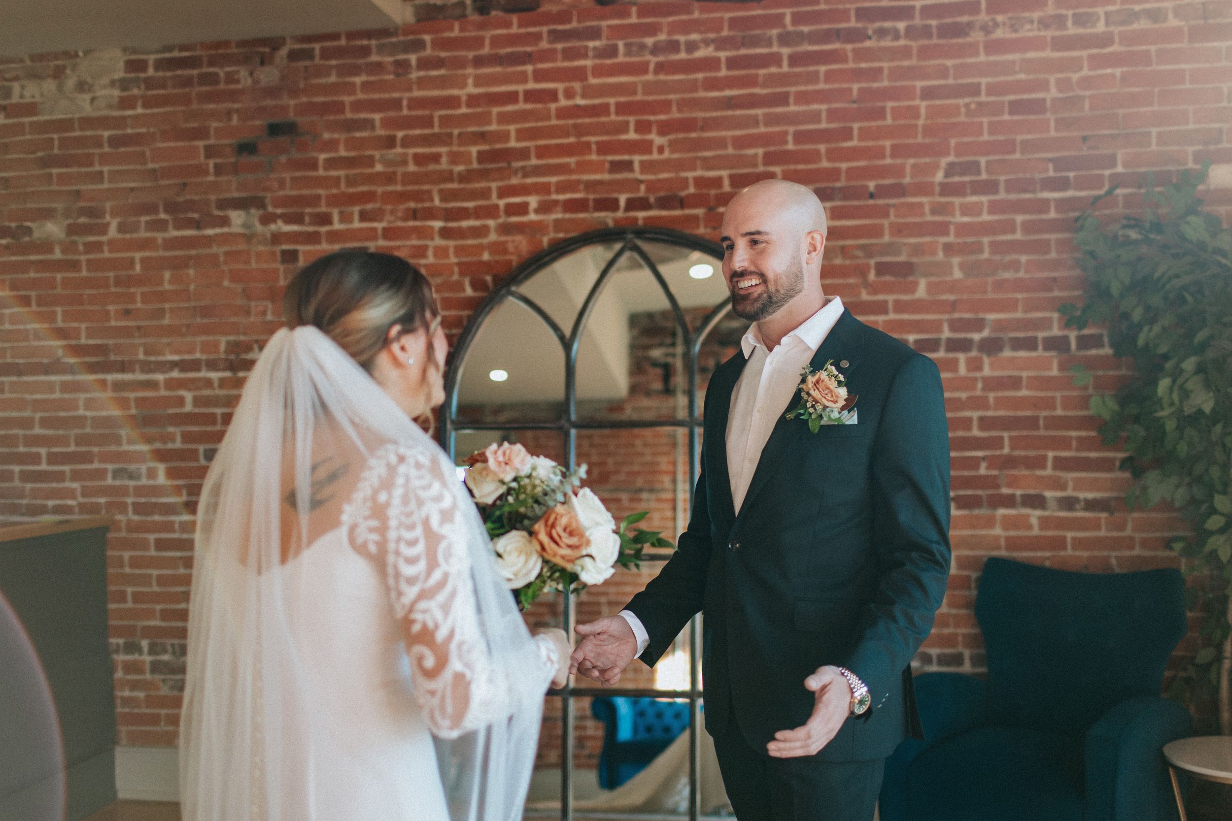 Candid first look reactions captured in rustic brick venue with natural window light.