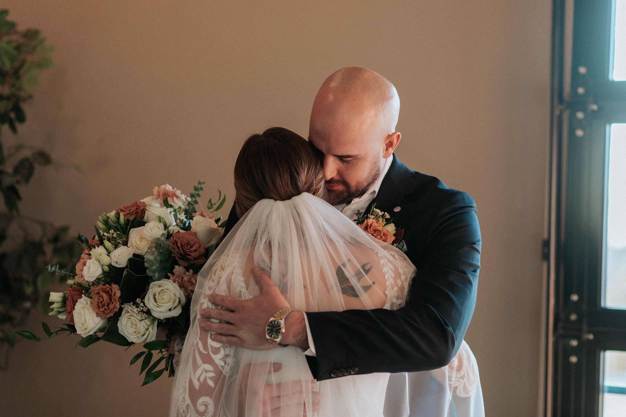 Emotional wedding first look captured in front of exposed brick wall with floral decor.