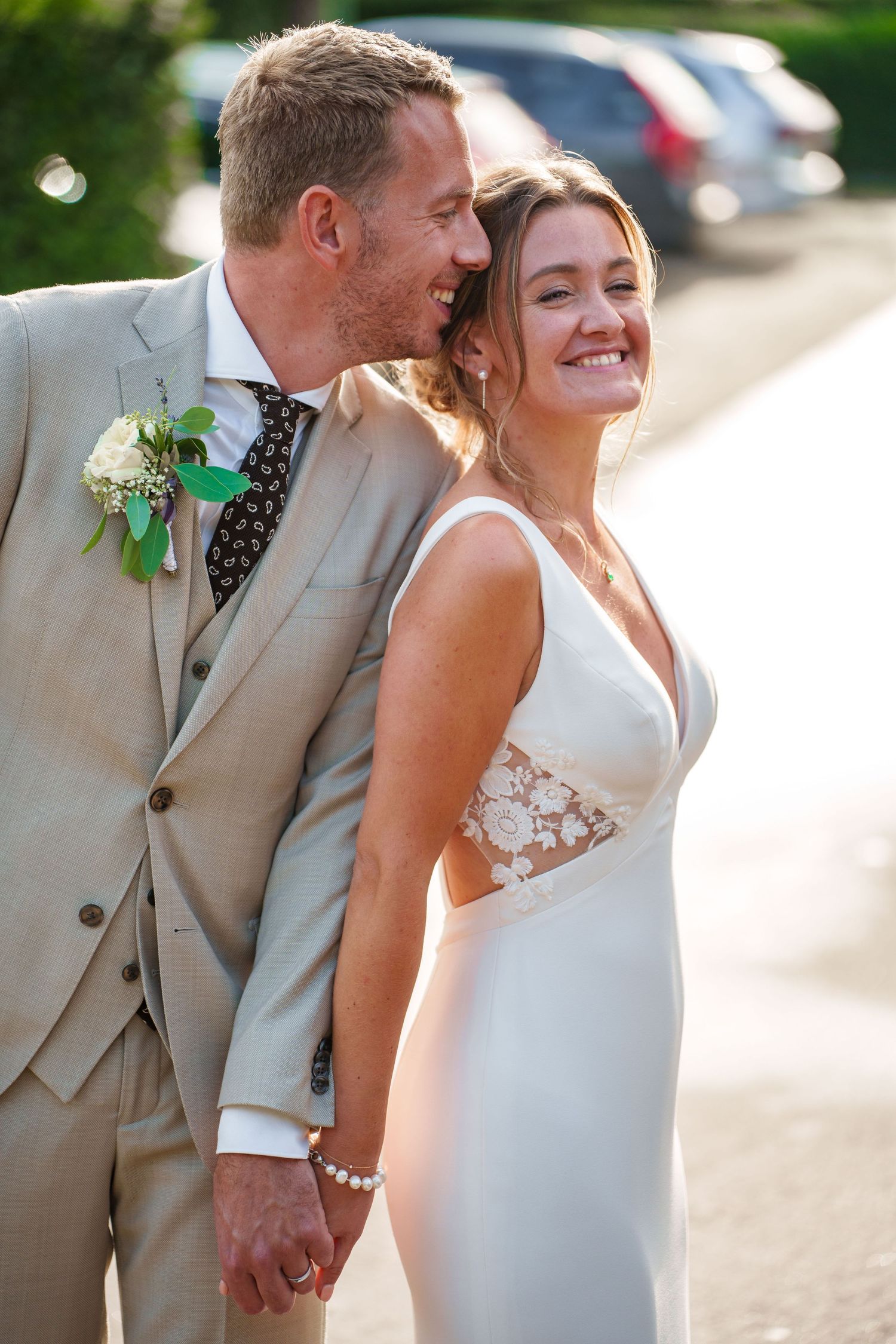 Happy couple in tan suit and white wedding dress sharing a joyful moment together outdoors.