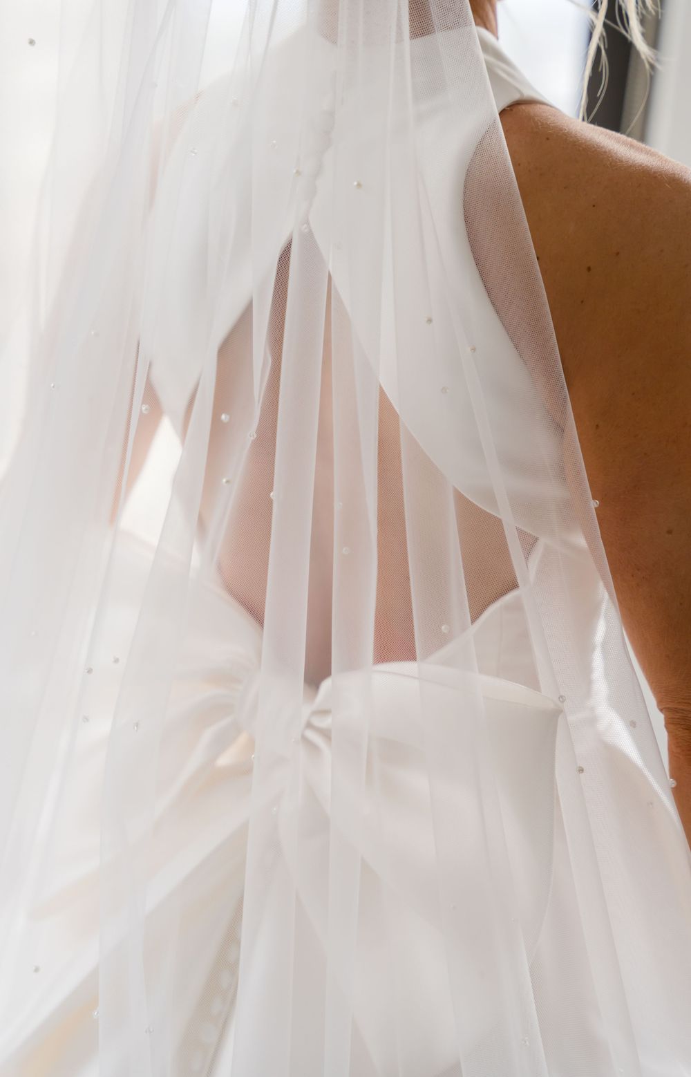 Delicate white wedding veil fabric flowing in a soft, ethereal pattern against a light background.