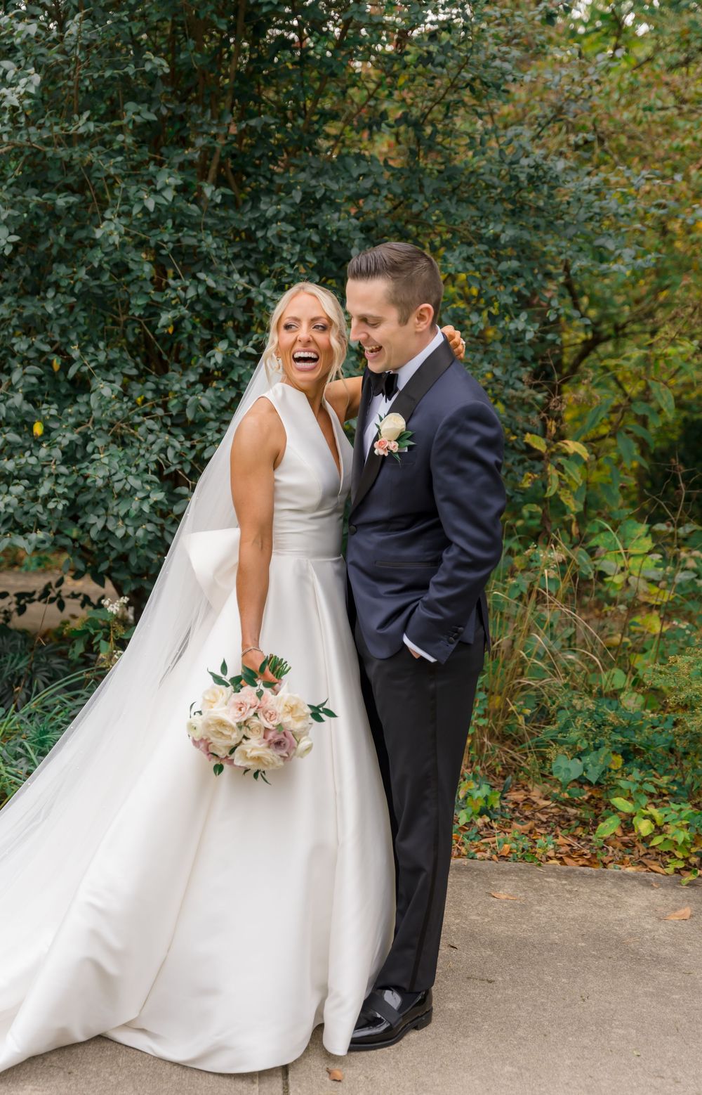 A joyful wedding moment captured outdoors with a bride in a classic white gown holding a pastel bouquet.