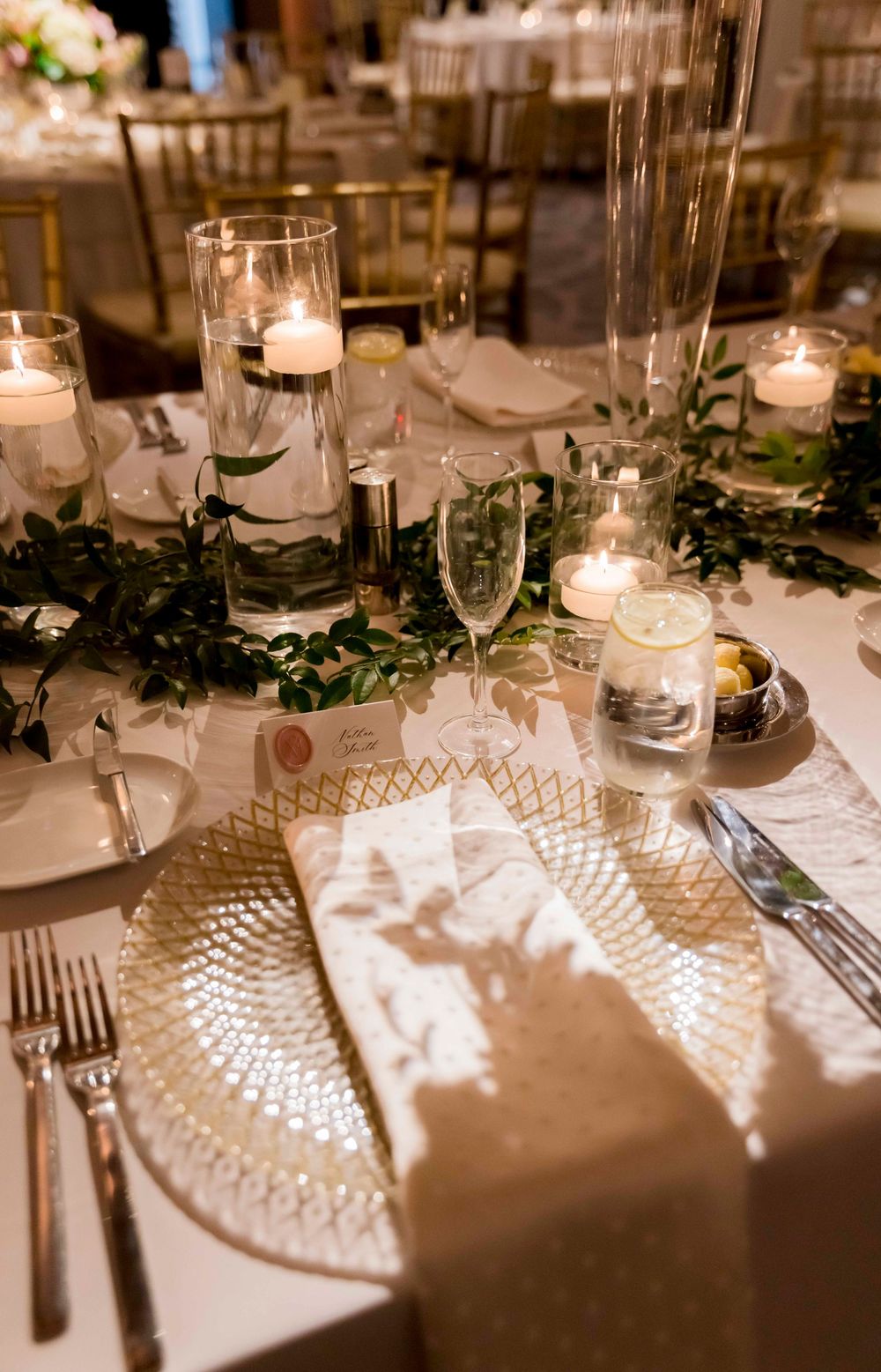 Elegant table setting with crystal plates, floating candles, and greenery garland at an upscale wedding reception.