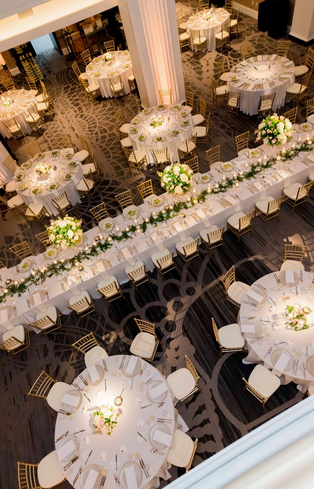 Elegant wedding reception setup with long white tables and floral centerpieces viewed from above.