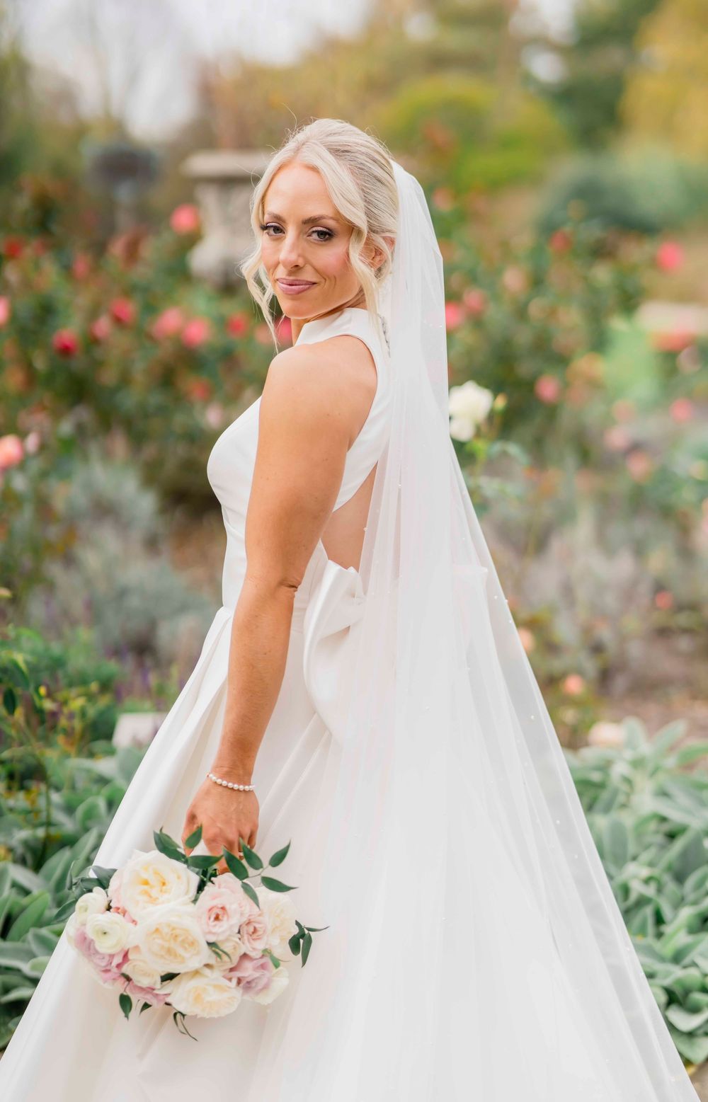 A bride in a classic white wedding gown poses in a garden setting with roses.