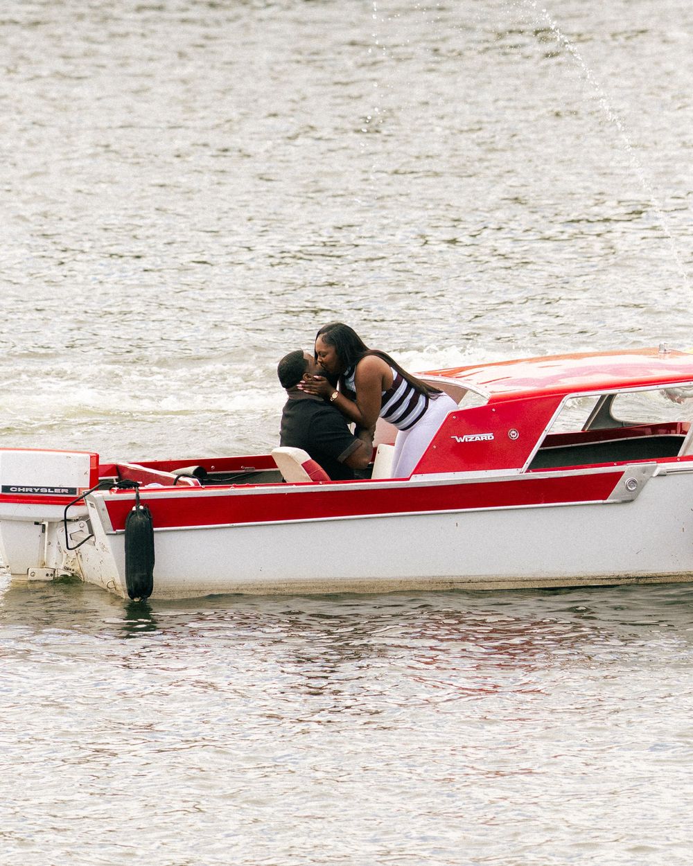 Couple sharing a romantic kiss on a red and white motorboat on calm water.
