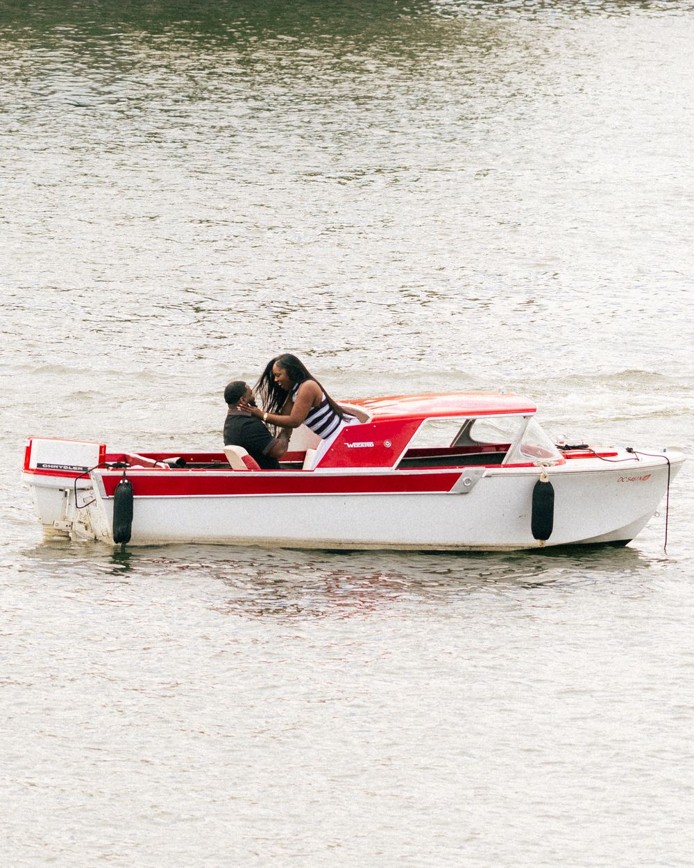 Couple sharing a romantic moment on a red and white motorboat on calm water.