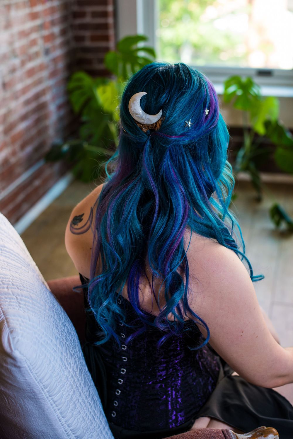 Close-up view of vibrant blue and purple dyed hair against a brick wall background.