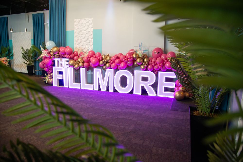 Illuminated 'FILLMORE' sign decorated with pink flowers and greenery.