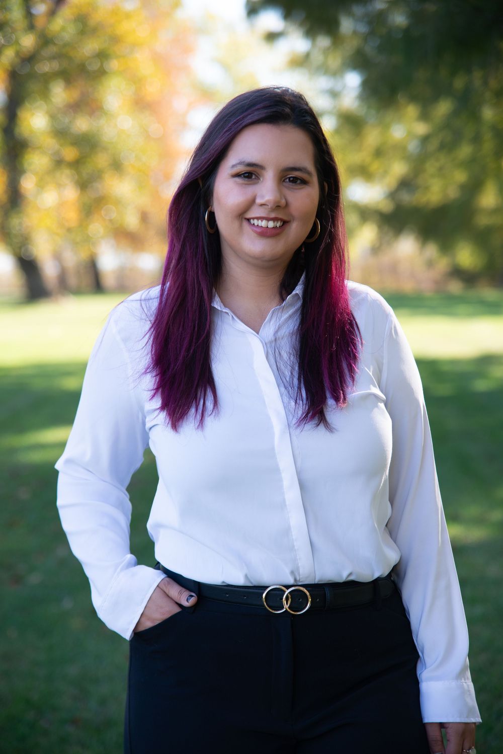 Professional portraits in white button-down shirt and black pants against autumn park scenery.