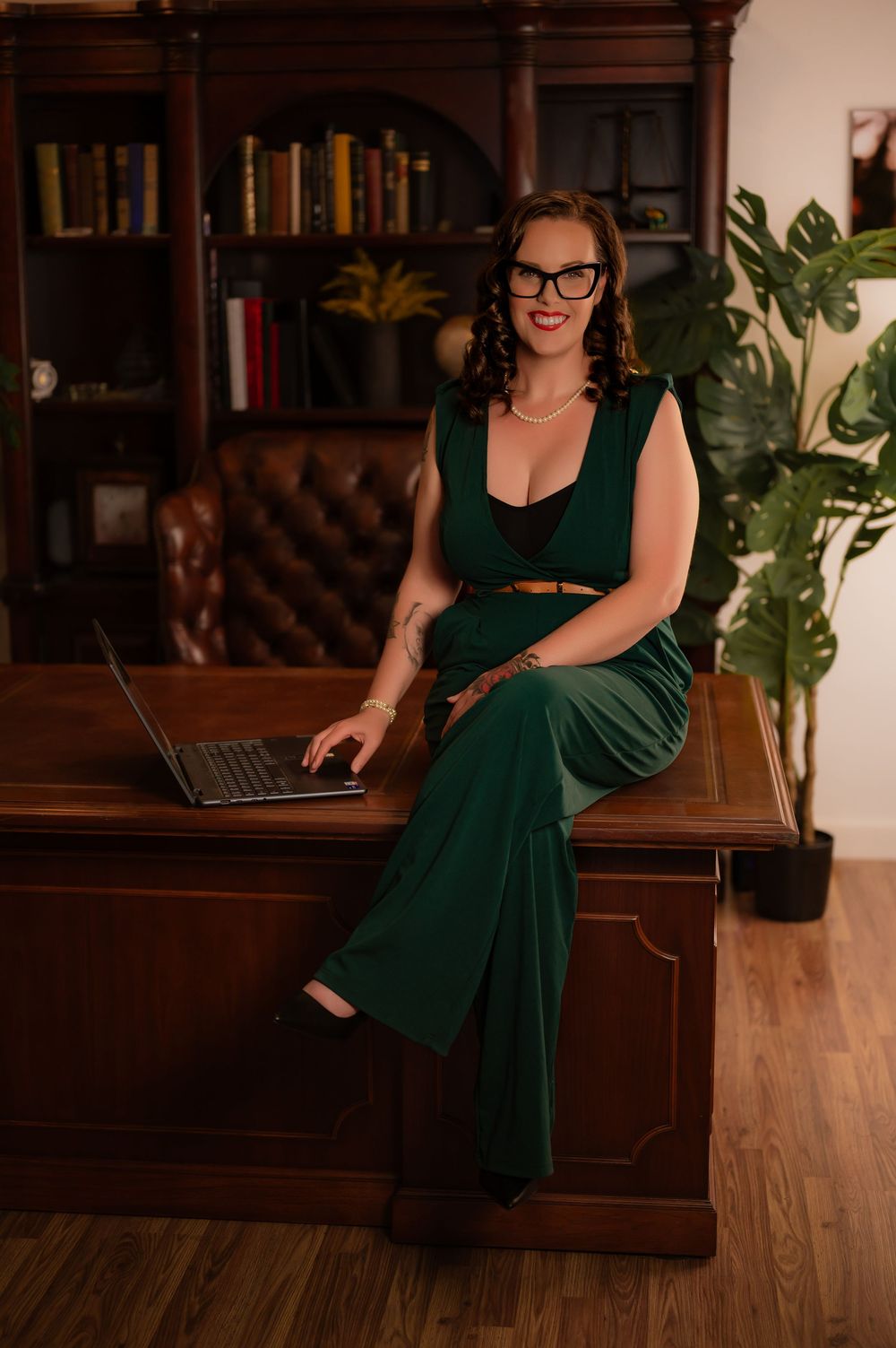 Elegant home office scene with emerald dress, laptop, and wooden furniture.